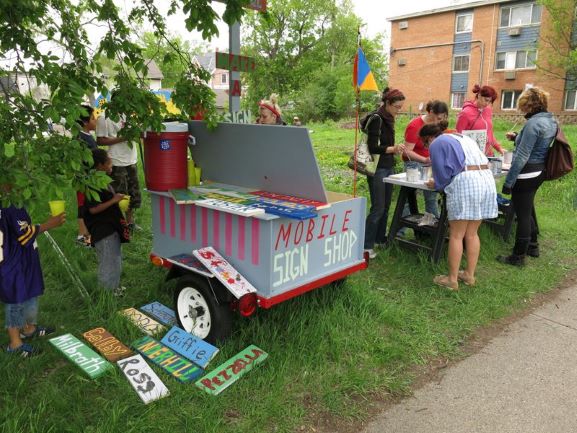 Group of people working on signs near a cute and colorful mobile sign shop trailer